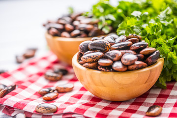 Uncooked beans in wooden bowles  with parsley herbs on kitchen table