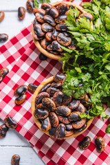 Uncooked beans in wooden bowles  with parsley herbs on kitchen table