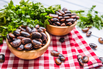 Uncooked beans in wooden bowles  with parsley herbs on kitchen table