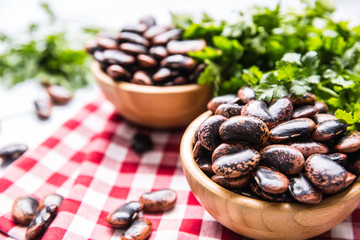 Uncooked beans in wooden bowles  with parsley herbs on kitchen table