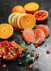 Slices of grapefruit, lemon and pomegranate in the black background.