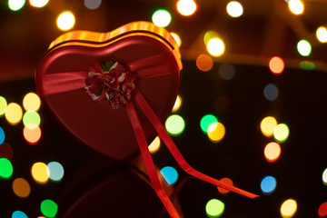 Red heart with a bow, on a dark background with lights, a gift for Valentine's Day. February 14 - Valentine's Day.