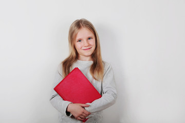 Little smiling beautiful girl standing and holding red book over grey  background 