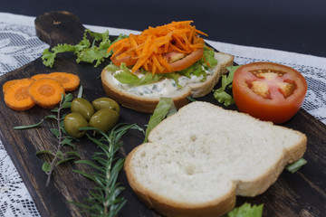 Healthy vegetarian sandwich with carrot, Tomato, lettuce and spices, served on an wooden board.