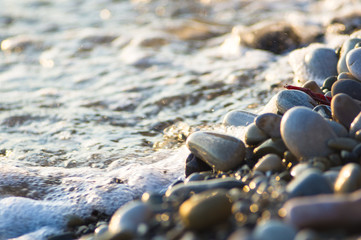 pebble stones on the sea beach, the rolling waves of the sea with foam
