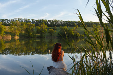 girl in dress sitting near a lake in nature