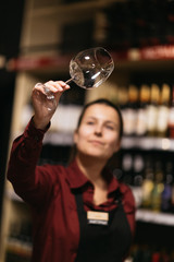 Picture of woman with wine glass on blurred background of shelves with bottles