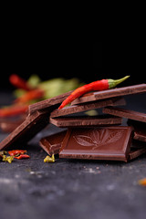 Natural black chocolate with red bitter pepper on a black background.