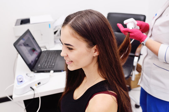 doctor dermatologist diagnoses the structure of the hair of a young pretty girl with a special tool - a trichoscope. Trichology, trichogram