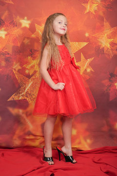pretty cute caucasian child girl in red evening dress and mother's high heels standing on orange background with stars