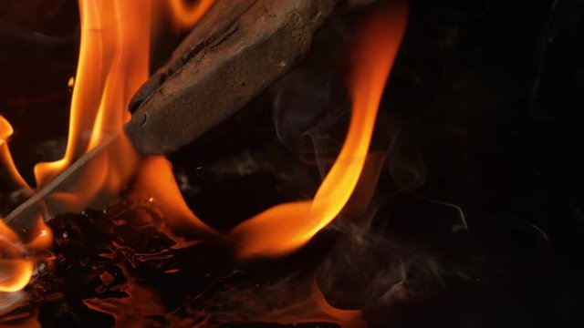 SLOW MOTION, MACRO, DOF: Rusty tongs holding a metal blade in oil during tempering procedure. Cinematic shot of fire being quenched as the burning piece of metal is dipped in water. Fire and smoke.
