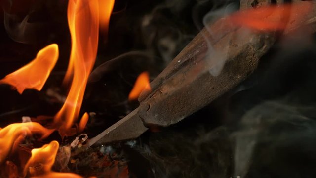 SLOW MOTION, MACRO, DOF: Burning blade held by bladesmith's tongs is swirled around the hot oil during heat treatment as the orange flames get put out and the smoke rises from the surface of the oil.