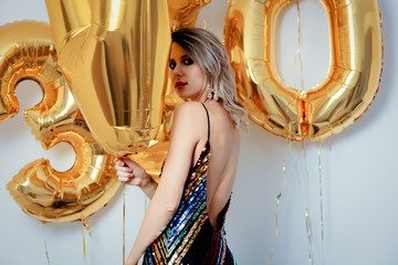 Young woman with golden balloons on her thirty years birthday. Indoor location. Person is in vintage 80th dress and hairstyle. On white background