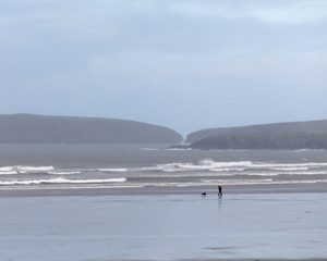 Man walking dog on beach in cold, windy winter UK