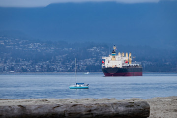 Cargo ship and yacht in Pacific ocean, view from the beach, with mountains and city on the background