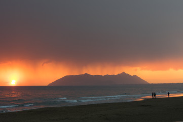 Obraz premium Rainy clouds with a red sunset sky in a seascape with Circeo in the background