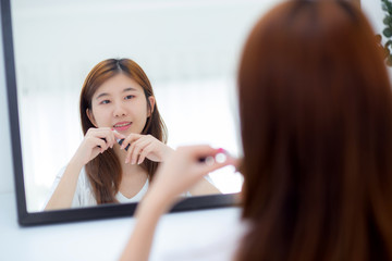 Beauty of portrait of young asian woman at the mirror holding and looking a makeup lipstick, Beautiful girl beauty fashion at the room, lifestyle concept.