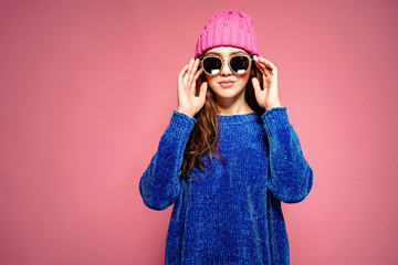 Modern young woman wearing blue sweater and pink hat posing, making funny facial expression.Retouched, studio portrait.