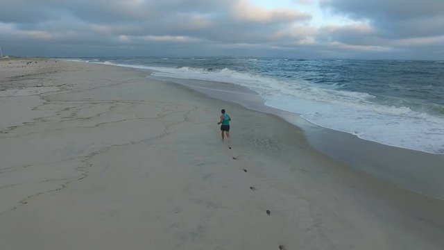 aerial view, young fit man during a morning run on the ocean beach