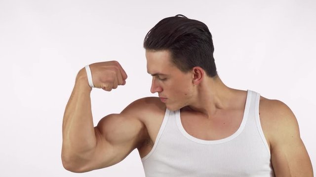 Muscular young man flexing his bicep looking to the camera fiercely. Handsome male bodybuilder showing off his muscles. Athletic man with huge biceps. Sports, determination, lifestyle concept