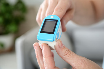 Mature woman checking pulse with medical device at home, closeup