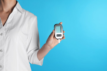 Female doctor holding digital glucometer on color background, closeup view with space for text. Medical object