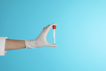 Female doctor holding empty test tube on color background, closeup view with space for text. Medical object