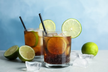 Glasses of cocktail with cola, ice and cut lime on table