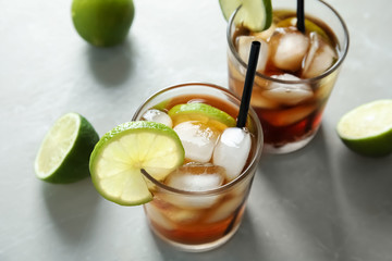Glasses of cocktail with cola, ice and cut lime on light background