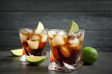 Glasses of cocktail with cola, ice and cut lime on table