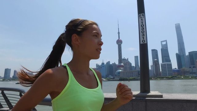 Asian woman running in city of Shanghai, China on famous boardwalk with skyline. Urban city lifestyle. Active woman runner exercising outside jogging on the Bund. Action camera