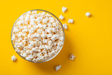 Glass bowl with salted popcorn on yellow background. Top view with copy space. Flat lay - obrazy, fototapety, plakaty