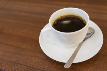 Close up hot espresso with bubbles in white coffee cup on wood table near window in coffee shop in the morning in vintage soft tone, black caffeine to stay awake for people