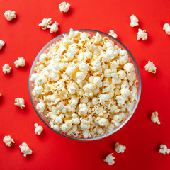 Fototapeta na wymiar Glass bowl of salty popcorn on a red background. Top view with copy space. Flat lay
