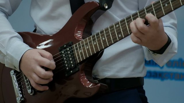 The guy pulls strings with a mediator and clamps his frets on a musical power tool. A teenager in a white shirt plays a brown electric guitar. Solo performance Concept musical theme of youth.