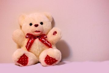 Cute valentine bear doll with bow isolated on white background with shadow reflection. Playful bright bear sitting on white underlay. Teddy bear plush stuffed puppet with ribbon on white backdrop