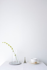 Glass vase of dried flower plant an eiffel tower miniature and a white vintage ceramic cup of coffee on white table top on white wall background with blank copy space for product mock up placement