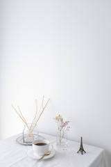 Glass vase of dried flower plant a vintage white ceramic cup of coffee an eiffel tower miniature on white table top on white wall background with blank copy space for product mock up placement 