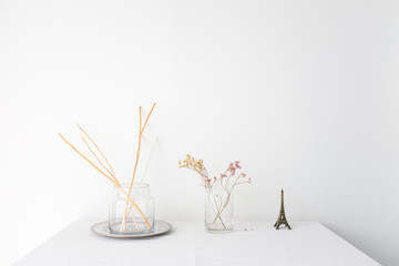 Glass vase of dried flower plant an eiffel tower miniature on white table top on white wall background with blank copy space for product mock up placement 
