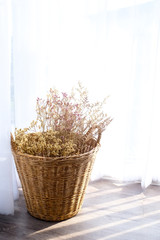 Dried plant and flower in rattan wooden basket on white table top on white curtain background in natural light