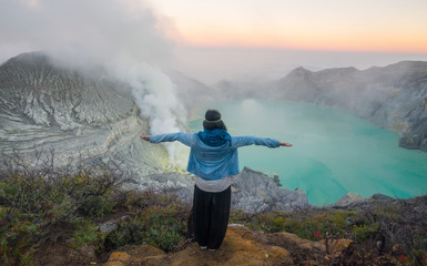 Back view of young woman standing on the crater of Kawah Ijen volcano in East Java, Indonesia.