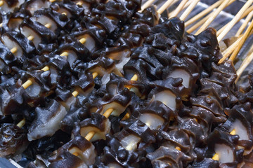 Fast food in the Asian market. Snack on wooden chopsticks resembles a sea cucumber prepared for frying