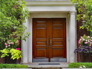 elegant double wooden front door and portico entrance surrounded by flowers of upper class house