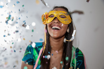 people, holidays, emotion and carnival concept - happy young woman with mask and confetti at...