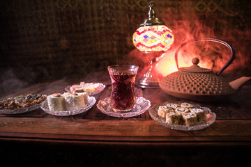 Arabian tea in glass with eastern snacks on vintage wooden surface. Eastern tea concept. Low light lounge interior with carpet. Empty space.