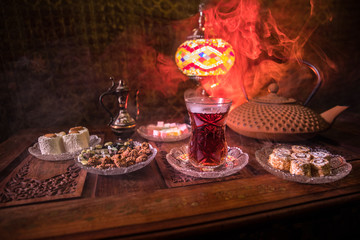 Arabian tea in glass with eastern snacks on vintage wooden surface. Eastern tea concept. Low light lounge interior with carpet. Empty space.