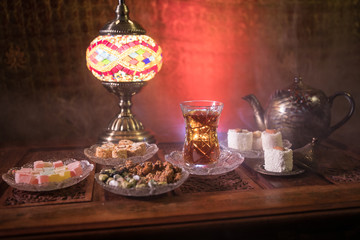 Arabian tea in glass with eastern snacks on vintage wooden surface. Eastern tea concept. Low light lounge interior with carpet. Empty space.