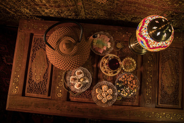 Arabian tea in glass with eastern snacks on vintage wooden surface. Eastern tea concept. Low light lounge interior with carpet. Empty space.