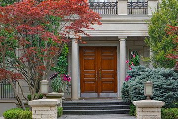 elegant double wooden front door and portico entrance surrounded by flowers of upper class house