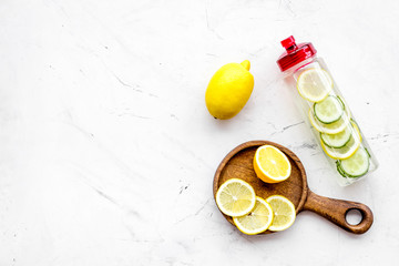 Detox infused water with slices of lemon and cucumber in bottle on white stone background top view space for text